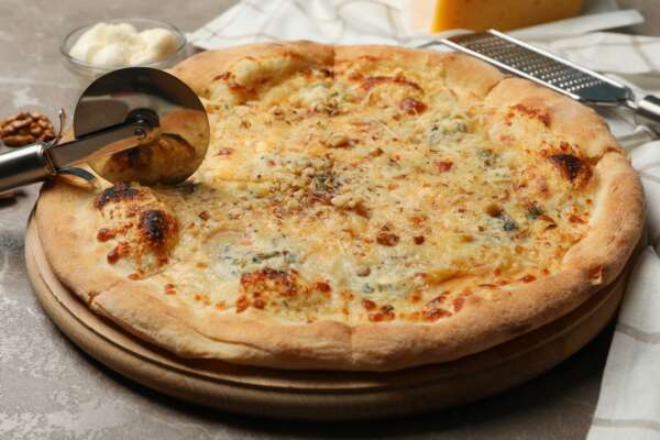 Pizza cutter and cheese pizza, close up